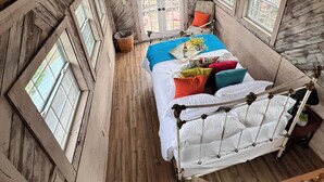 A cozy attic bedroom with a bed, a hanging chair, and a window. - Romantic getaway in the trees.  Enjoy your stay in a majestic oak treehouse (Celeste)