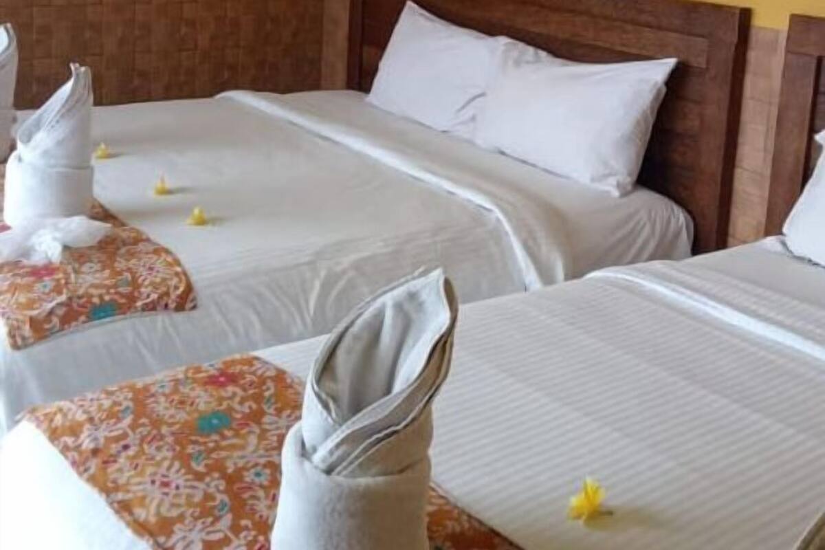 A hotel room with two beds, each with white linens and pillows, a wooden headboard, and a floral-patterned table runner.