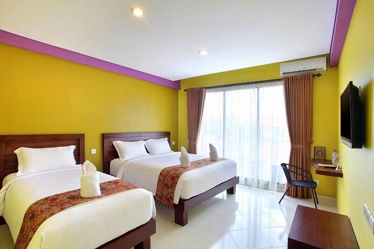 A hotel room with two beds, a desk, a chair, and a TV.
