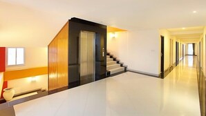 Un interior moderno con una escalera, un ascensor de vidrio y un pasillo que conduce a otra habitación.