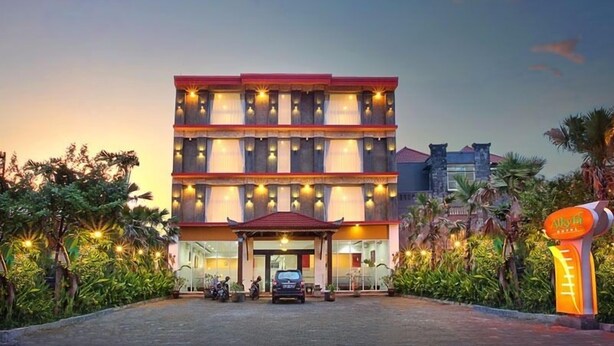 Un hotel de varios pisos con techo rojo y ventanas iluminadas, rodeado de abundante vegetación.