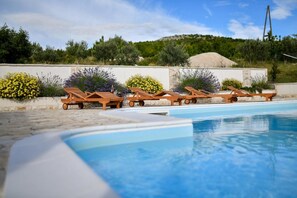 Un espace piscine doté de chaises longues en bois et d’un mur en pierre.