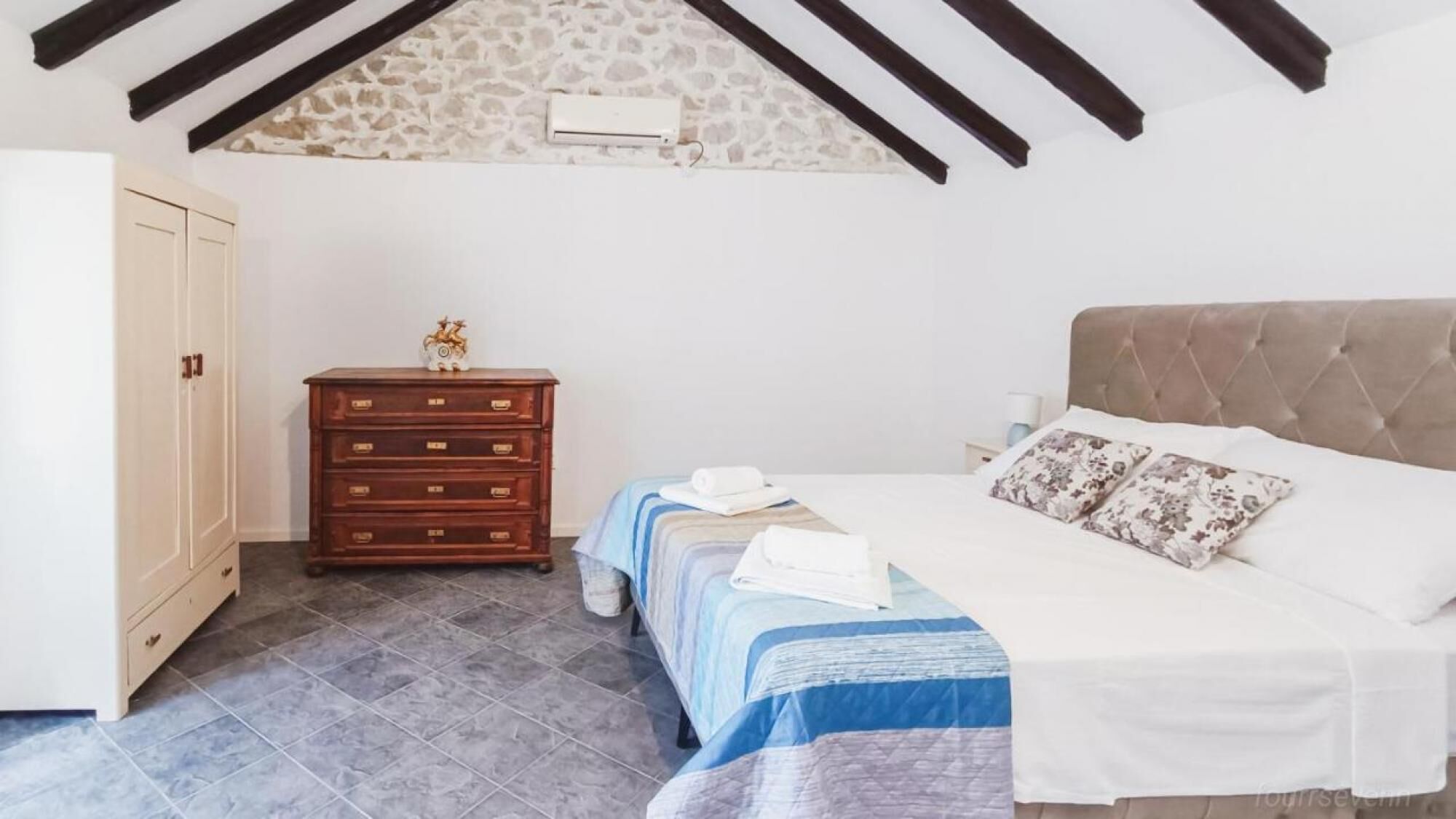 A bedroom with a bed, a dresser, and a stone wall.