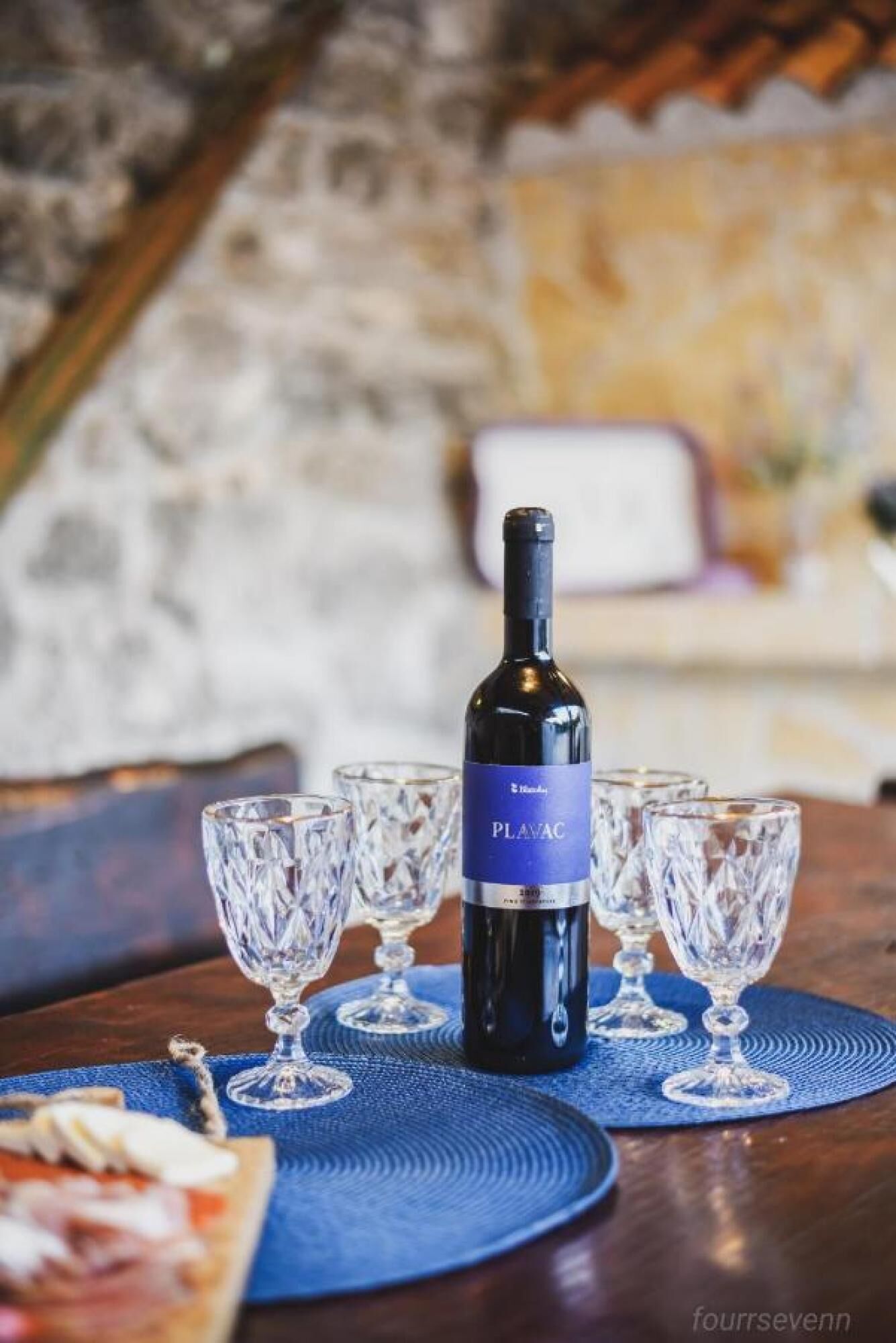 A bottle of Plavac wine on a table with four crystal wine glasses.
