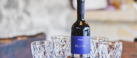 A bottle of Plavac wine on a table with four crystal wine glasses.