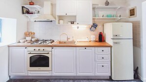 A compact kitchen with white cabinets, a gas stove, a built-in oven, a sink, and a white refrigerator. - Didini Dvori in Kru evo (Obrovac)
