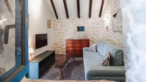 A rustic stone-walled room with a wooden ceiling, a blue sofa, a wooden cabinet, and a television. - Didini Dvori in Kru evo (Obrovac)