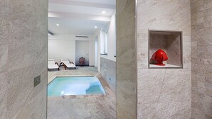 Zona d'una piscina interior moderna amb aigua cristal·lina, gandules i un objecte vermell decoratiu en un nínxol.