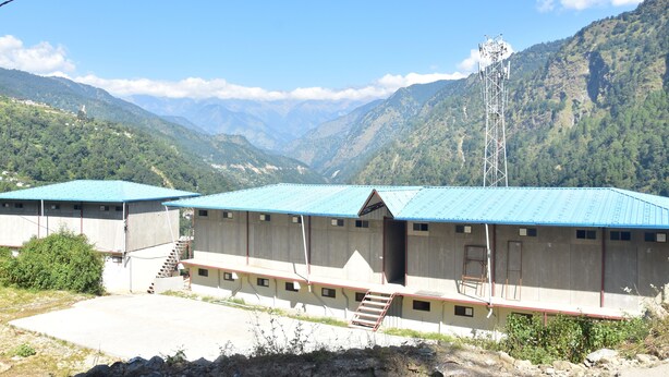 A building with a blue roof, a staircase, and a view of mountains. - Hotel Anandam Phata (Ukhimath)