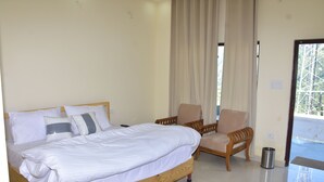 A bedroom with a wooden bed, a chair, a small trash bin, and a view of the outside. - Hotel Anandam Phata (Ukhimath)