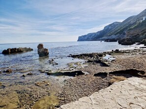 A rocky shoreline with clear water and a distant cliff.