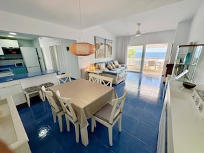 A modern kitchen with white cabinets, a dining table with chairs, and a view of the ocean through large windows.