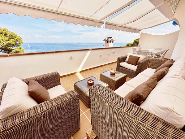 An outdoor seating area with wicker furniture and a view of the sea.