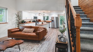 A modern kitchen with white cabinets, stainless steel appliances, and a wooden staircase.