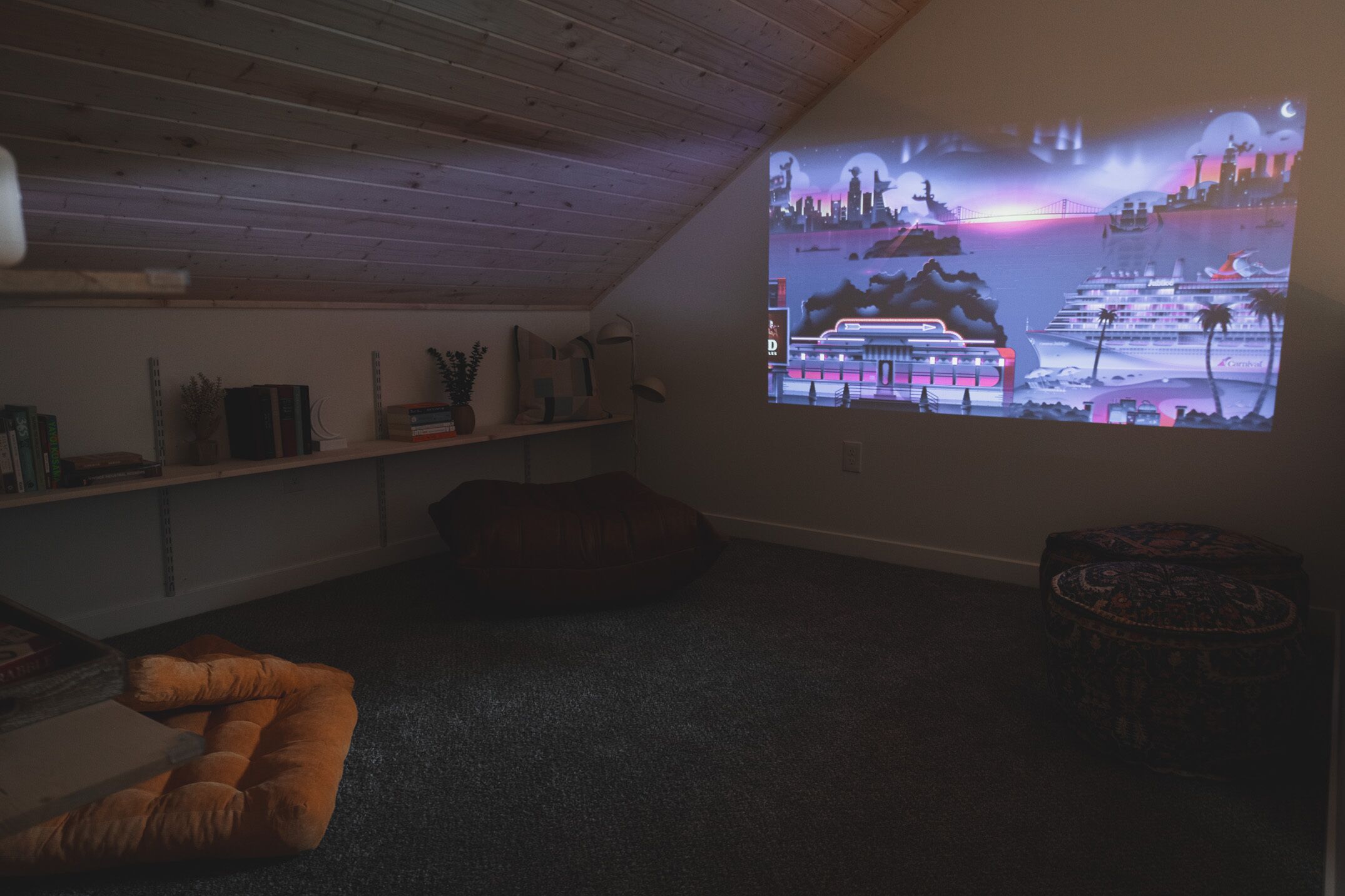 Una habitación acogedora con una amplia pantalla de proyección que muestra un paisaje urbano. Hay un sillón de peluche, un reposapiés pequeño y redondo, y una estantería con diversos objetos.