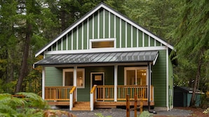 A green wooden cabin with a porch, a small window, and a door.