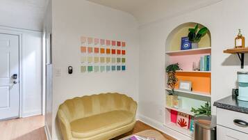 A room with a yellow sofa, a small round table with magazines, a bookshelf with various items, and a door.