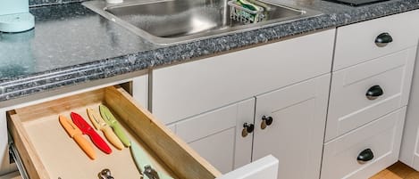 A kitchen with a sink, a coffee maker, and a drawer with various kitchen utensils.
