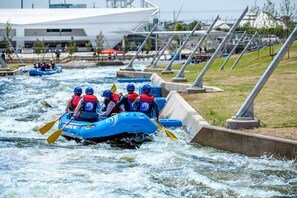 Eine Gruppe von Menschen treibt auf einem Fluss, im Hintergrund ein modernes Gebäude.