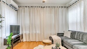Ein modernes Wohnzimmer mit einem grauen Sofa, einem runden Couchtisch, einem Fernseher auf einem Holzständer und einem Deckenventilator.