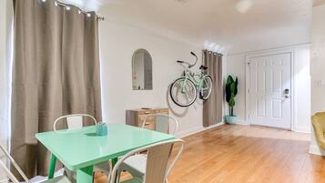 Una habitación con una mesa de comedor, sillas, una bicicleta colgada en la pared, una puerta y una planta en maceta.