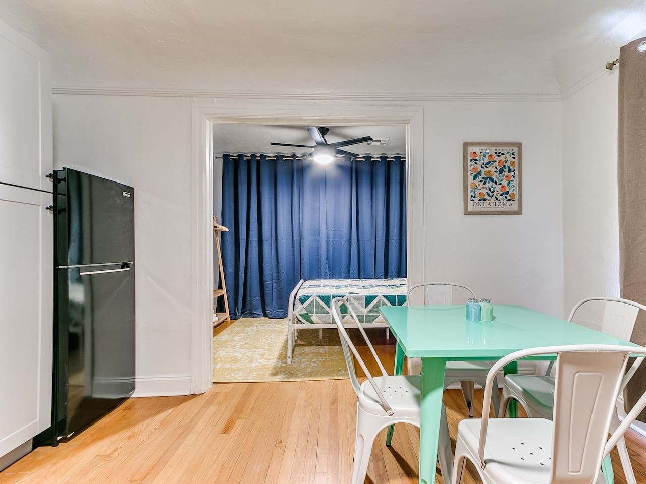 A room with a dining table, chairs, a ceiling fan, and a refrigerator.