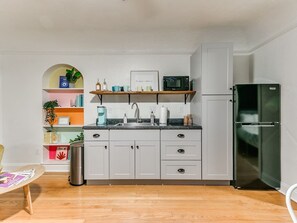 Une cuisine de taille réduite avec des meubles gris, un évier en acier inoxydable et un réfrigérateur noir.