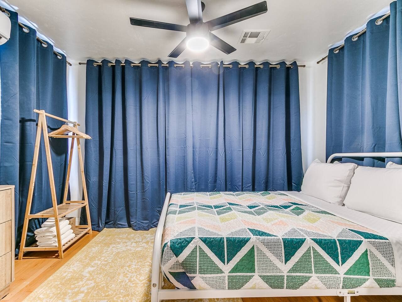 A bedroom with a bed, a ceiling fan, and a wooden shelf with towels.