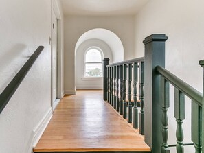 Un couloir doté d’un plancher en bois, de murs blancs et d’une rambarde verte.