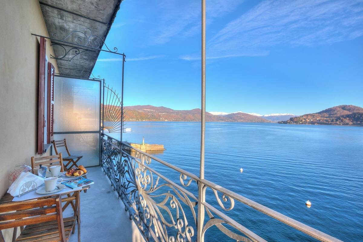A balcony with a table set for breakfast, overlooking a calm lake with mountains in the distance.