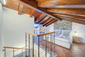 A bedroom with a stone wall, a bed, a nightstand, and a wooden ceiling. - Aparthotel Arona (Arona)