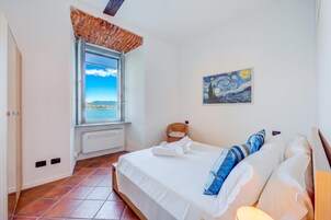 A bedroom with a bed, a window with a view, a painting on the wall, and a radiator.
