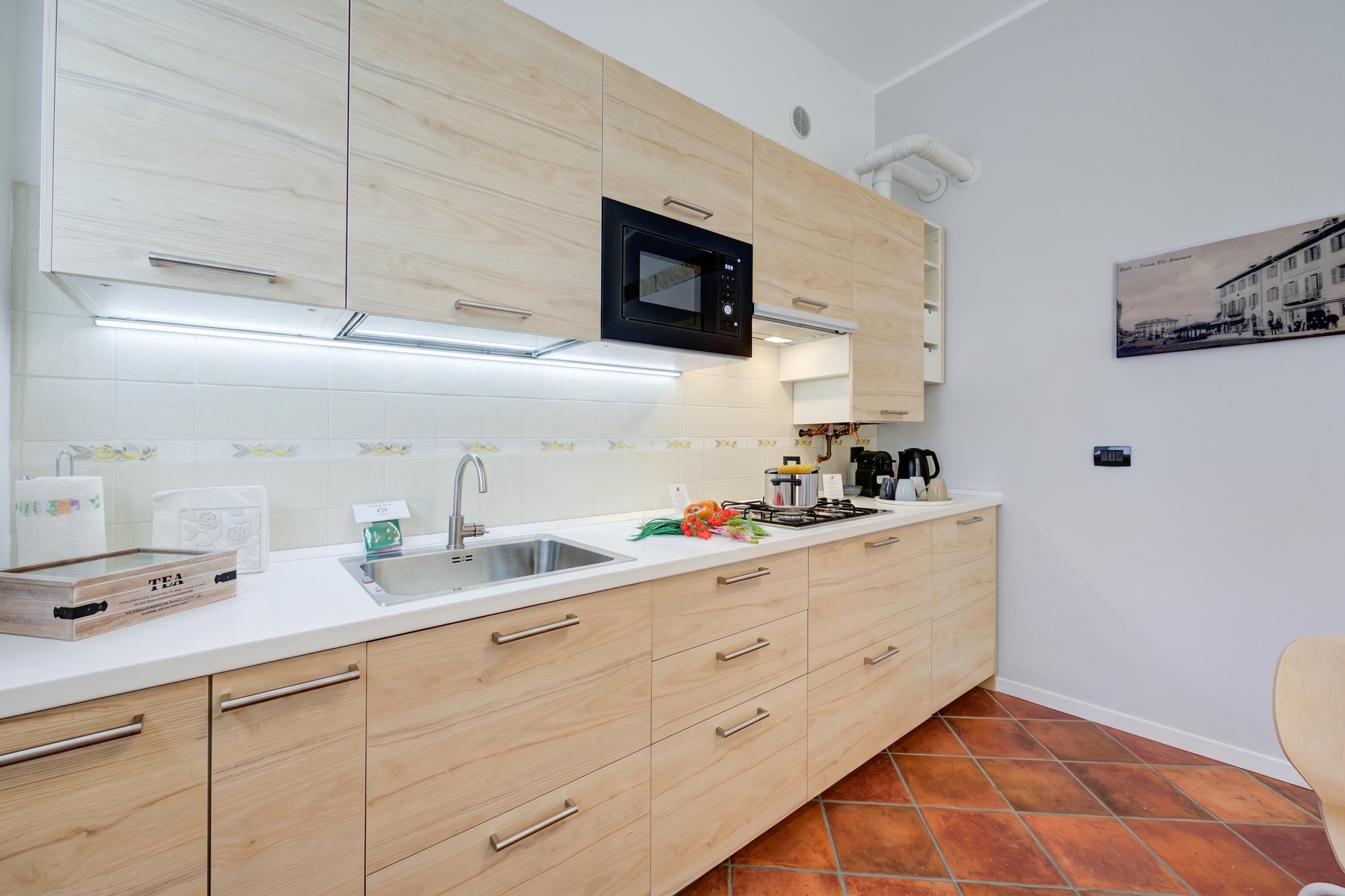 Una cocina moderna con armarios de madera, un microondas integrado, un lavamanos y una encimera con diversos objetos.