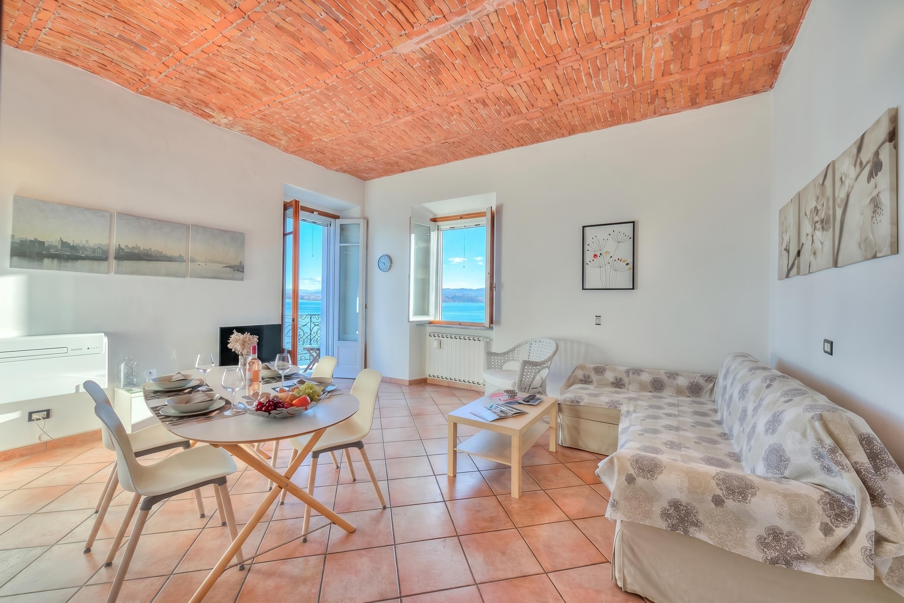 A living room with a dining area, a sofa, a coffee table, and a view of the sea.