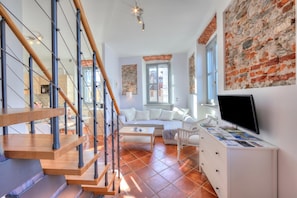 Uma sala de estar moderna com escada, sofá, mesa de centro e televisão sobre um armário branco.