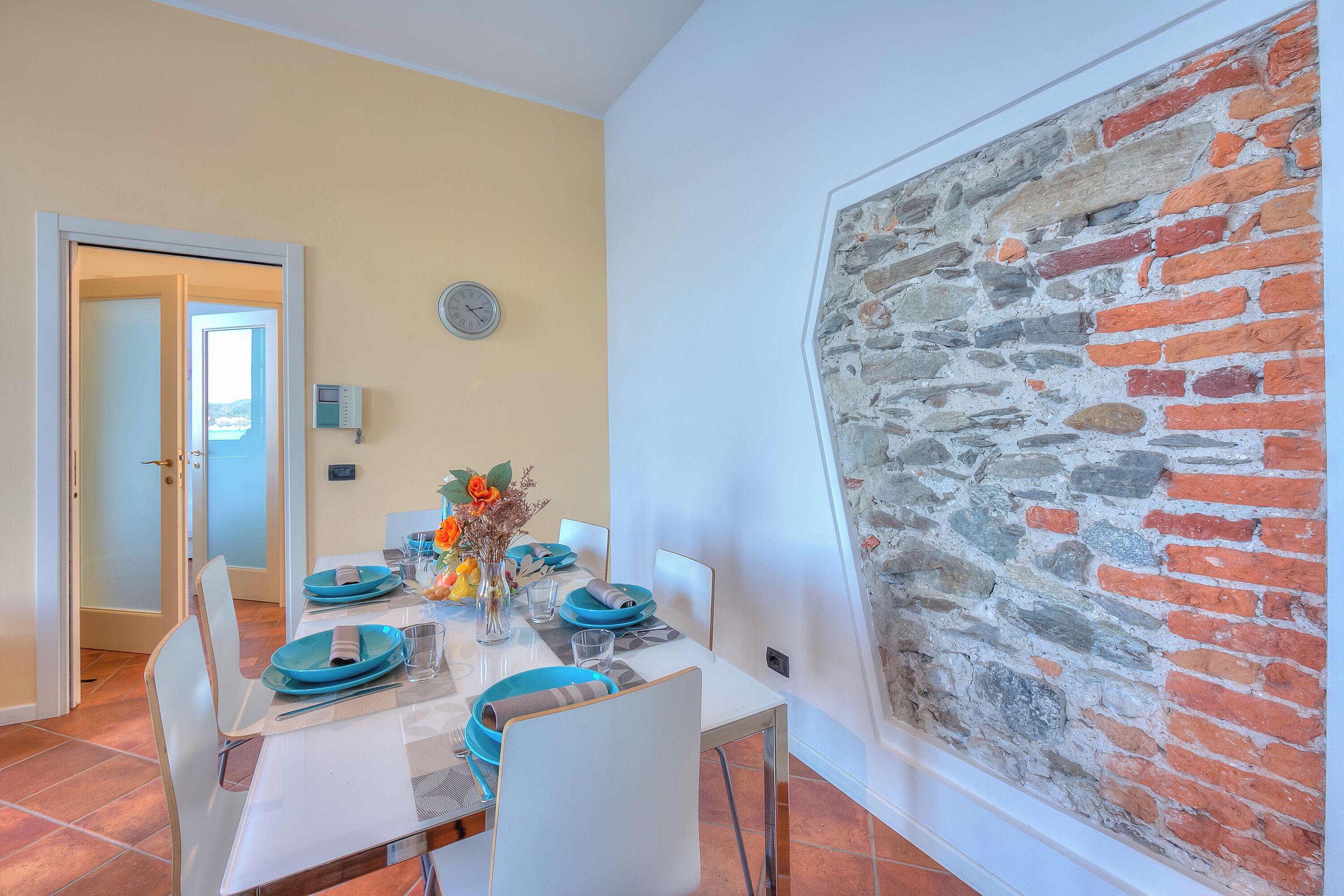 A dining area with a white table set for four, blue plates, and a vase with flowers.