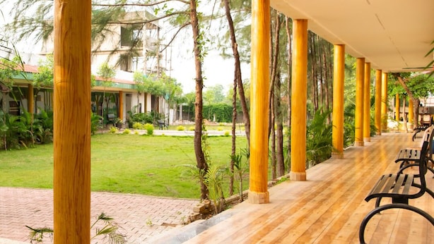Un espacio al aire libre cubierto con suelo de madera y pilares amarillos, bancos y vistas a un edificio y vegetación.
