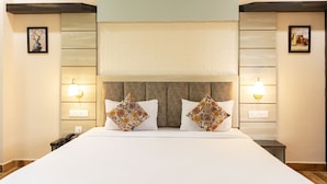 Una habitación de hotel con una cama grande, dos mesitas de noche, un cabecero de madera y lámparas fijadas a la pared.