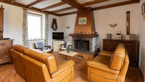 A cozy living room with leather sofas, a fireplace, wooden beams, a television, and a vintage radio. - Esprit Bailly by Interhome (Cancale)