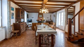 A dining area with a wooden table set for four, flanked by wooden chairs. A chandelier hangs from the ceiling, and a staircase is visible to the right. - Esprit Bailly by Interhome (Cancale)