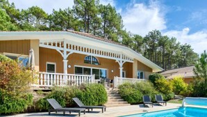 A two-story house with a pool, surrounded by trees and a patio area with lounge chairs.