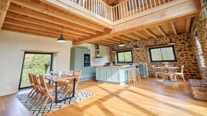 A spacious loft-style room with a high ceiling, exposed wooden beams, a central island with bar stools, and large windows offering views of the outdoors. - La Favrais by Interhome (Saint aubin de terregatte)