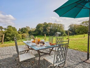 Un espace de restauration en plein air avec une table dressée pour quatre personnes, entourée de chaises, et protégée par un grand parasol.