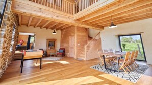 A spacious loft-style room with a high ceiling, exposed wooden beams, a dining area with a table and chairs, and a staircase leading to an upper level. - La Favrais by Interhome (Saint aubin de terregatte)