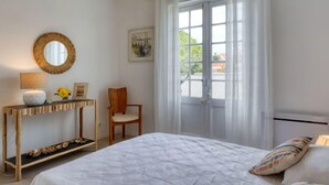 Una camera da letto con un letto, un comodino con una lampada, una sedia, una finestra con tende e uno specchio fissato al muro.