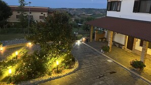 A residential area with a paved driveway, a well-lit garden with flowering plants, and a view of distant hills. - La Vigna di Ranco Ltd N3352 (Paglieta)