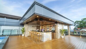 Un espace bar extérieur moderne, doté d’un comptoir en marbre, de tabourets de bar en bois et d’une piscine en arrière-plan.