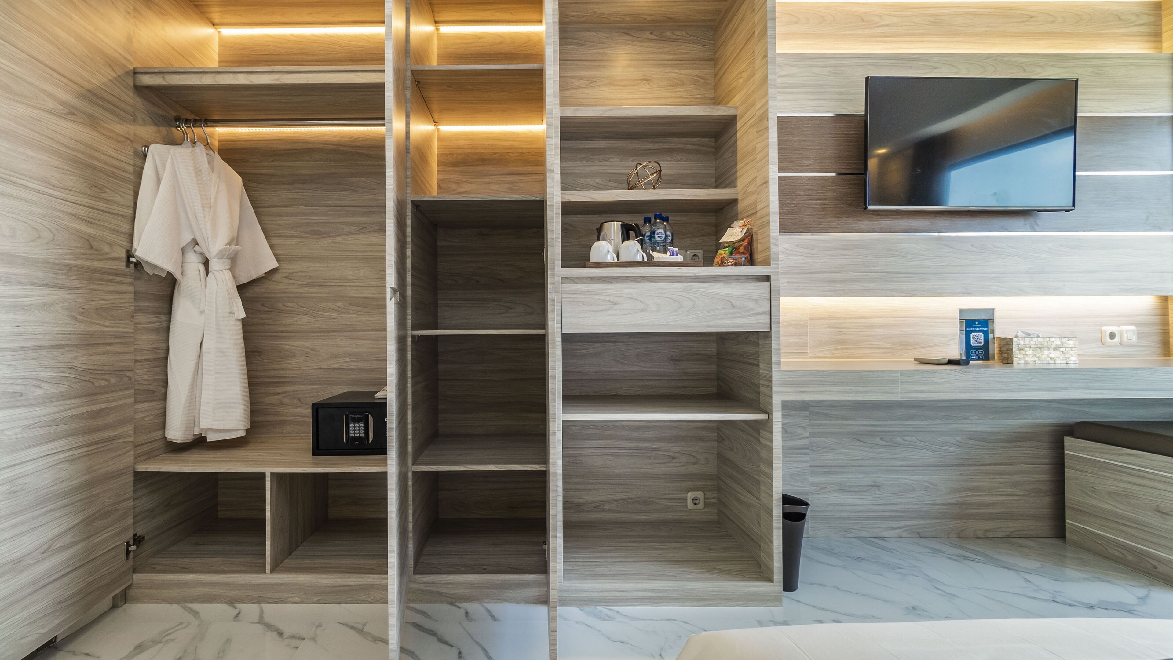 A modern bathroom with a wooden vanity, a robe hanging, a TV mounted on the wall, and a marble floor.