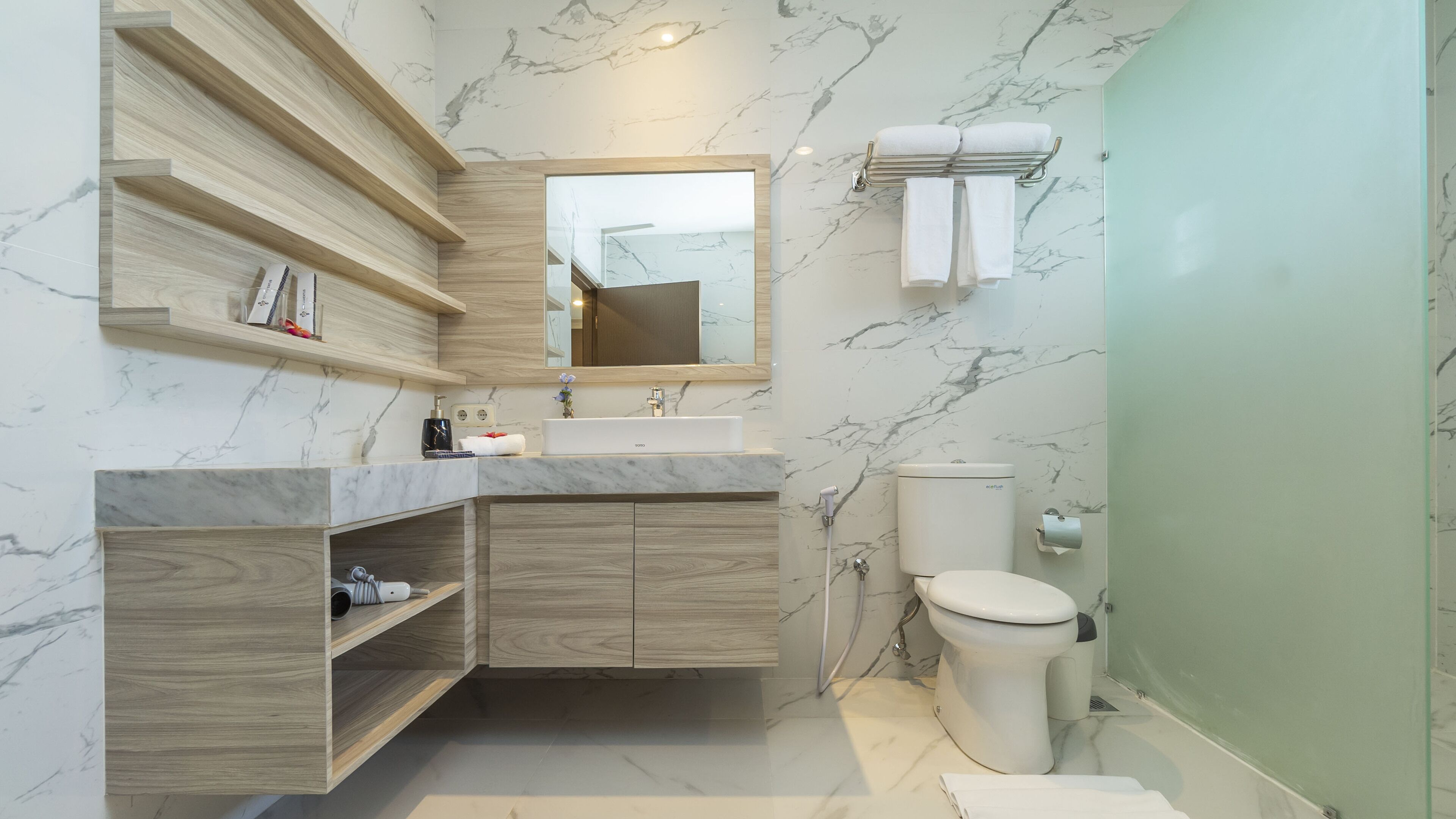 A modern bathroom with a marble backsplash, wooden vanity, a large mirror, and a toilet.