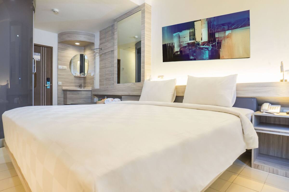 Ein modernes Hotelzimmer mit einem großen Bett, einem Nachttisch mit Lampe, einem Spiegel und einem Gemälde an der Wand.